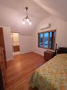 Bedroom with light wood-style flooring, vaulted ceiling, a chandelier, an AC wall unit, and connected bathroom