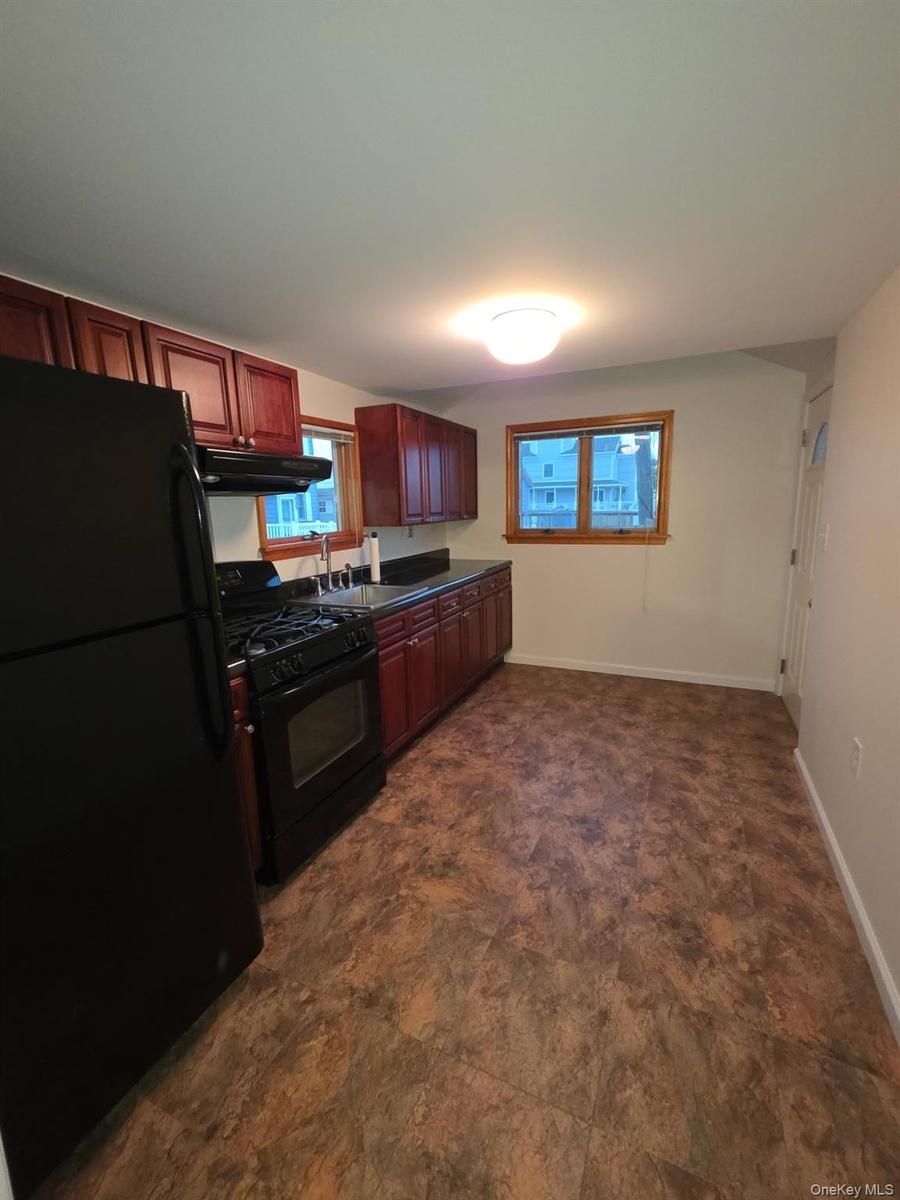 Kitchen featuring black appliances, dark countertops, under cabinet range hood, dark brown cabinets, and stone finish flooring