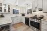 Kitchen with gas stove, glass insert cabinets, under cabinet range hood, hanging light fixtures, and black dishwasher