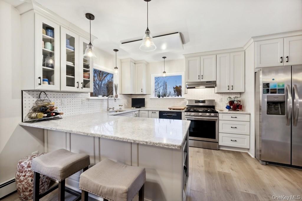 Kitchen featuring stainless steel appliances, light stone countertops, a peninsula, and white cabinetry