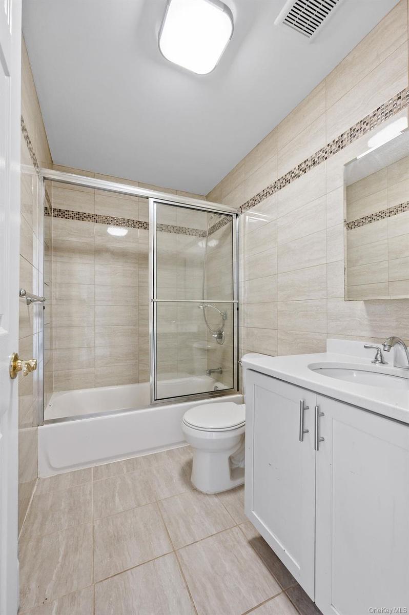Full bath featuring vanity, enclosed tub / shower combo, and tile walls