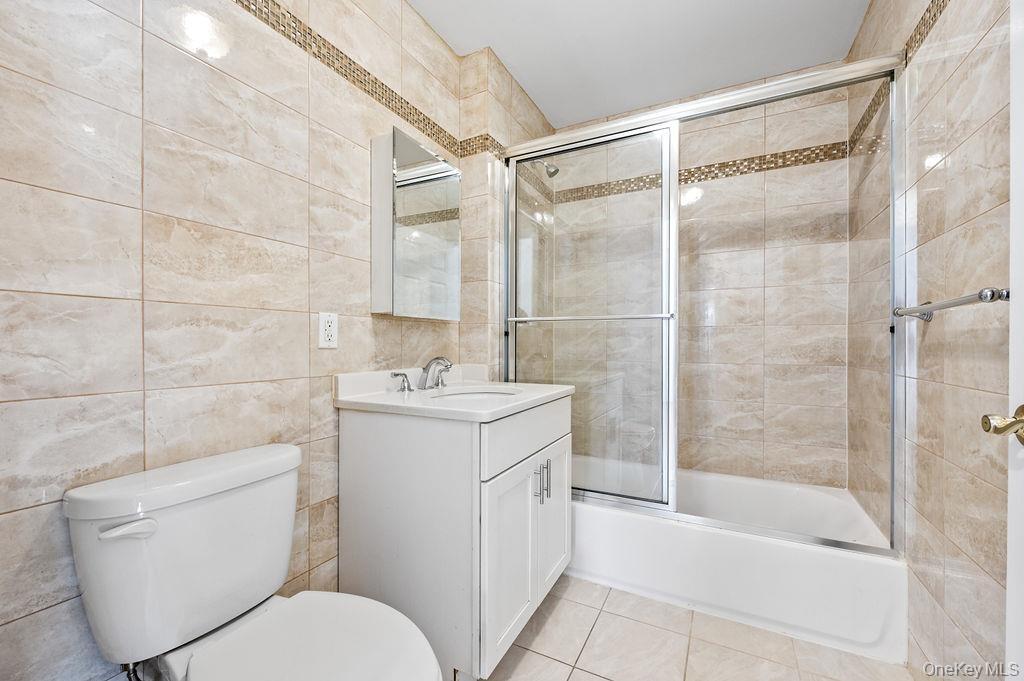Full bathroom featuring tile walls, vanity, and combined bath / shower with glass door