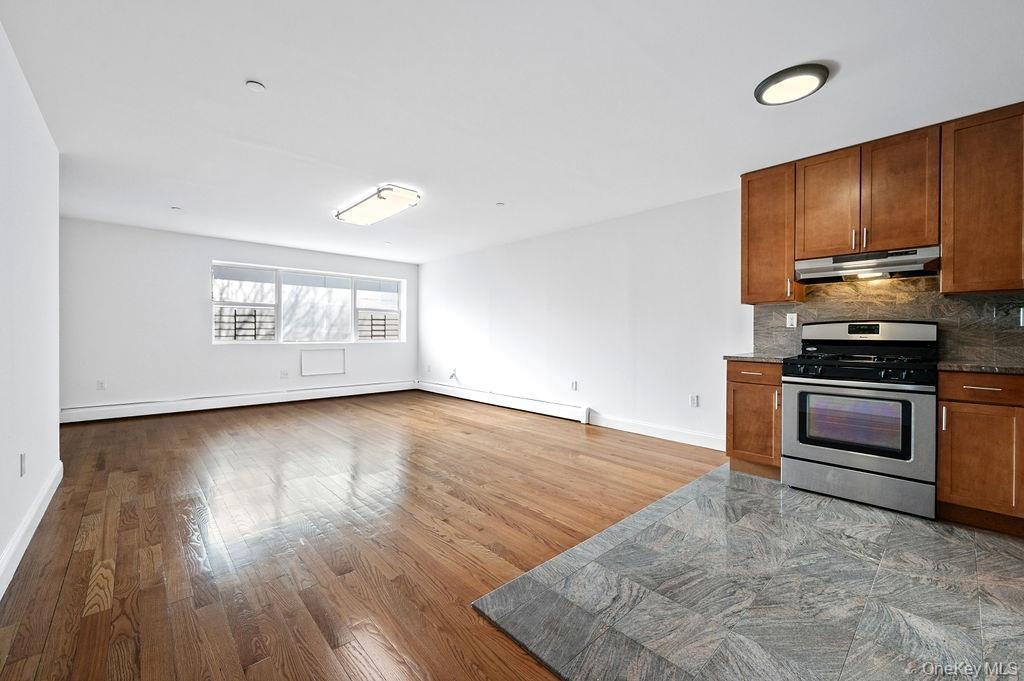Kitchen with gas stove, under cabinet range hood, open floor plan, backsplash, and wood finished floors