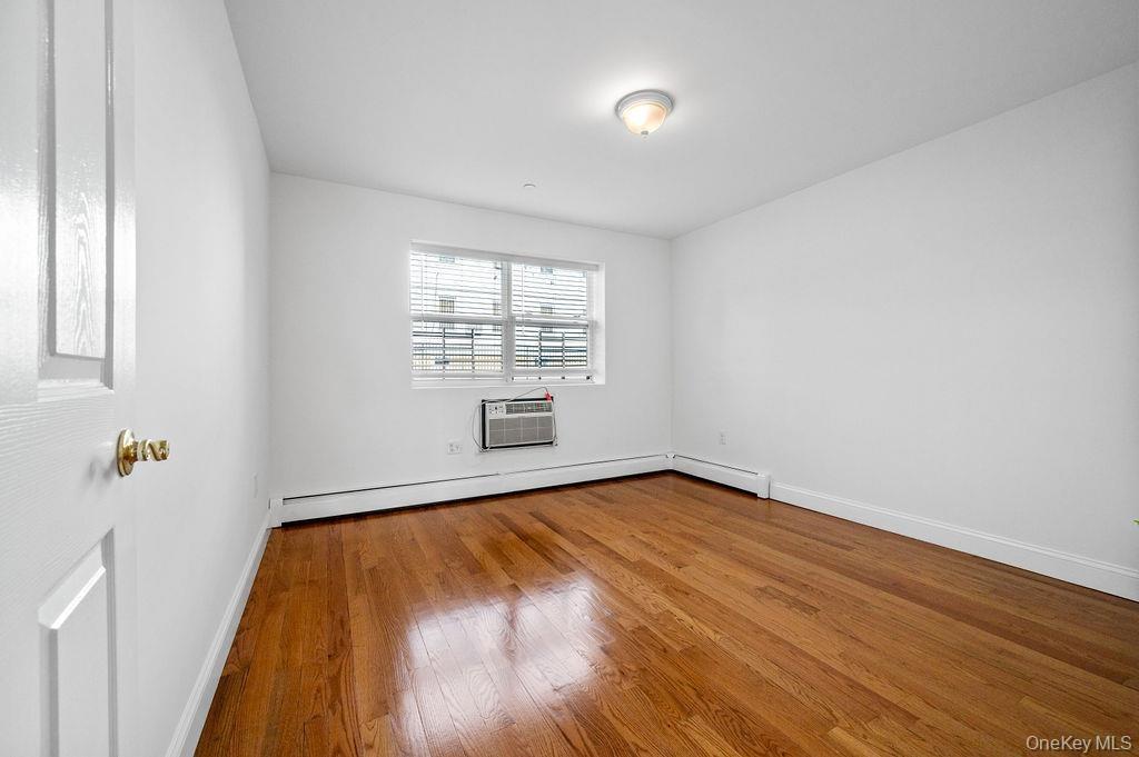 Empty room with baseboard heating, wood finished floors, and a wall mounted AC