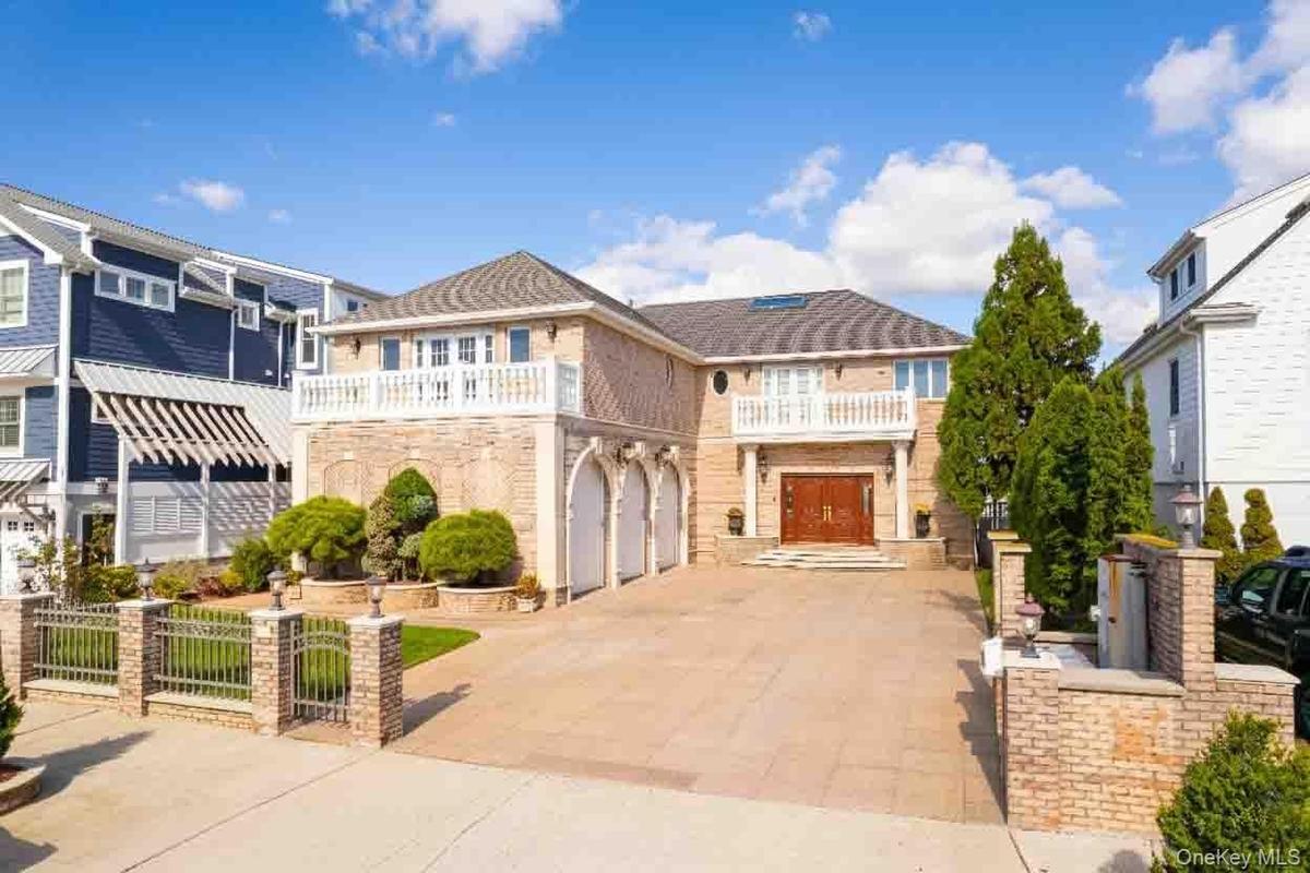 View of front of property with a balcony, driveway, a gate, stone siding, and a garage