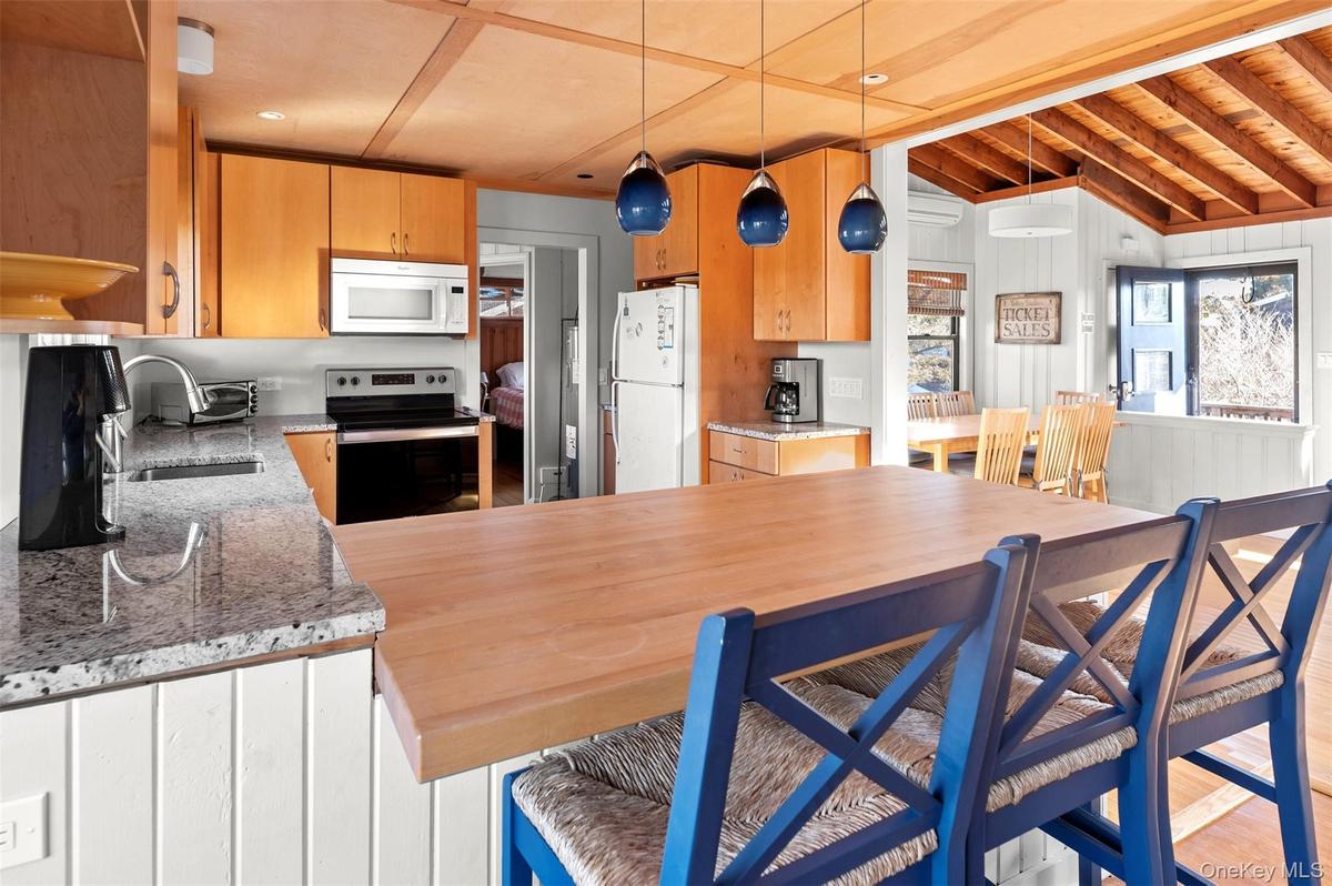 Kitchen with white appliances, light stone countertops, hanging light fixtures, a wooden ceiling with exposed beams, and light wood-type flooring