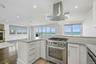 Kitchen featuring stainless steel appliances, white cabinetry, island exhaust hood, light wood-type flooring, and ornamental molding