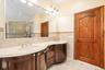 Full bathroom with double vanity, tile walls, tile patterned floors, tiled shower, and wainscoting