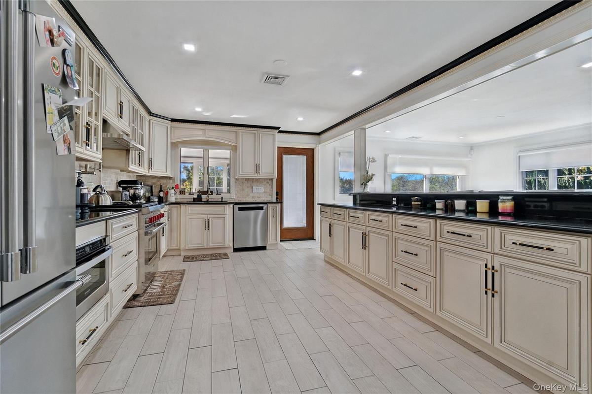 Kitchen featuring glass insert cabinets, stainless steel appliances, tasteful backsplash, cream cabinetry, and dark stone counters