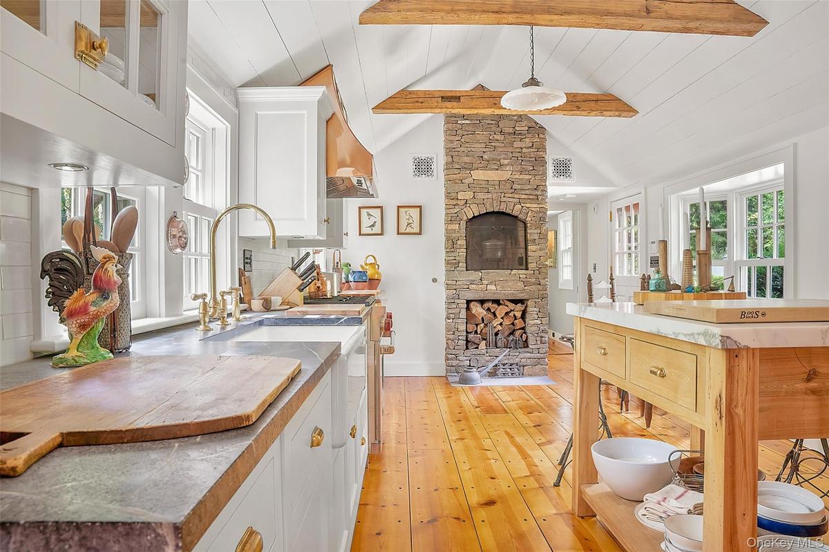 Kitchen with white cabinets, plenty of natural light, light wood-style flooring, a stone fireplace, and beamed ceiling