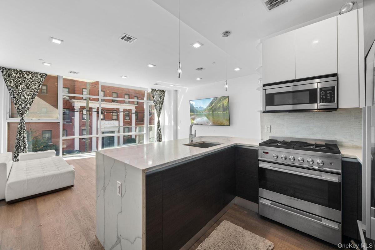 Kitchen featuring stainless steel appliances, modern cabinets, a peninsula, light stone countertops, and recessed lighting