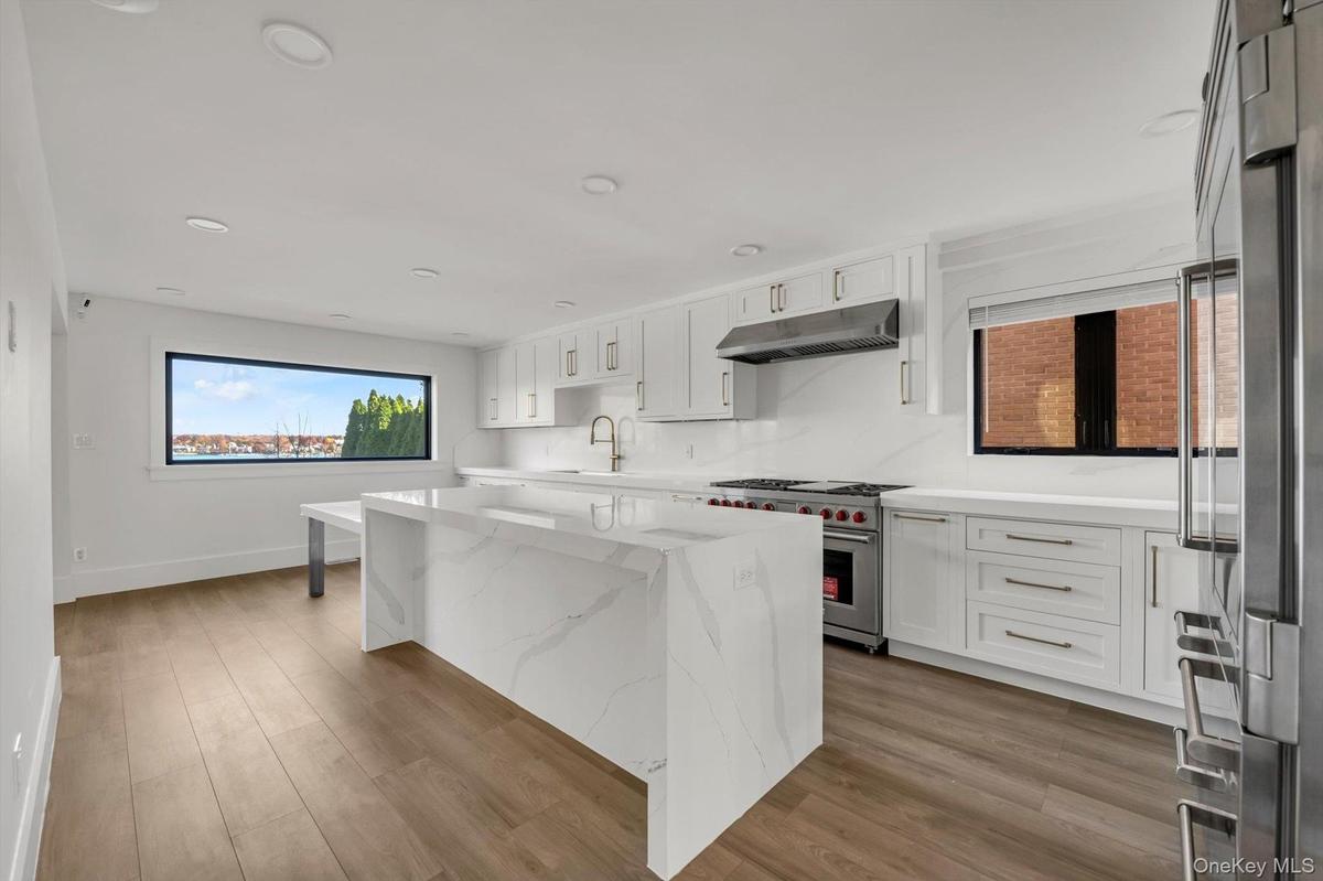 Kitchen featuring white cabinetry, light stone counters, high end appliances, a center island, and recessed lighting