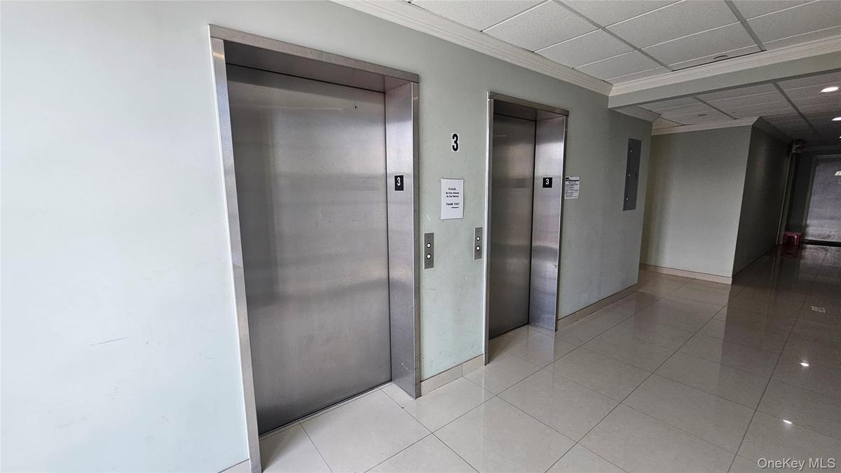 Corridor featuring elevator, tile patterned floors, crown molding, and a paneled ceiling