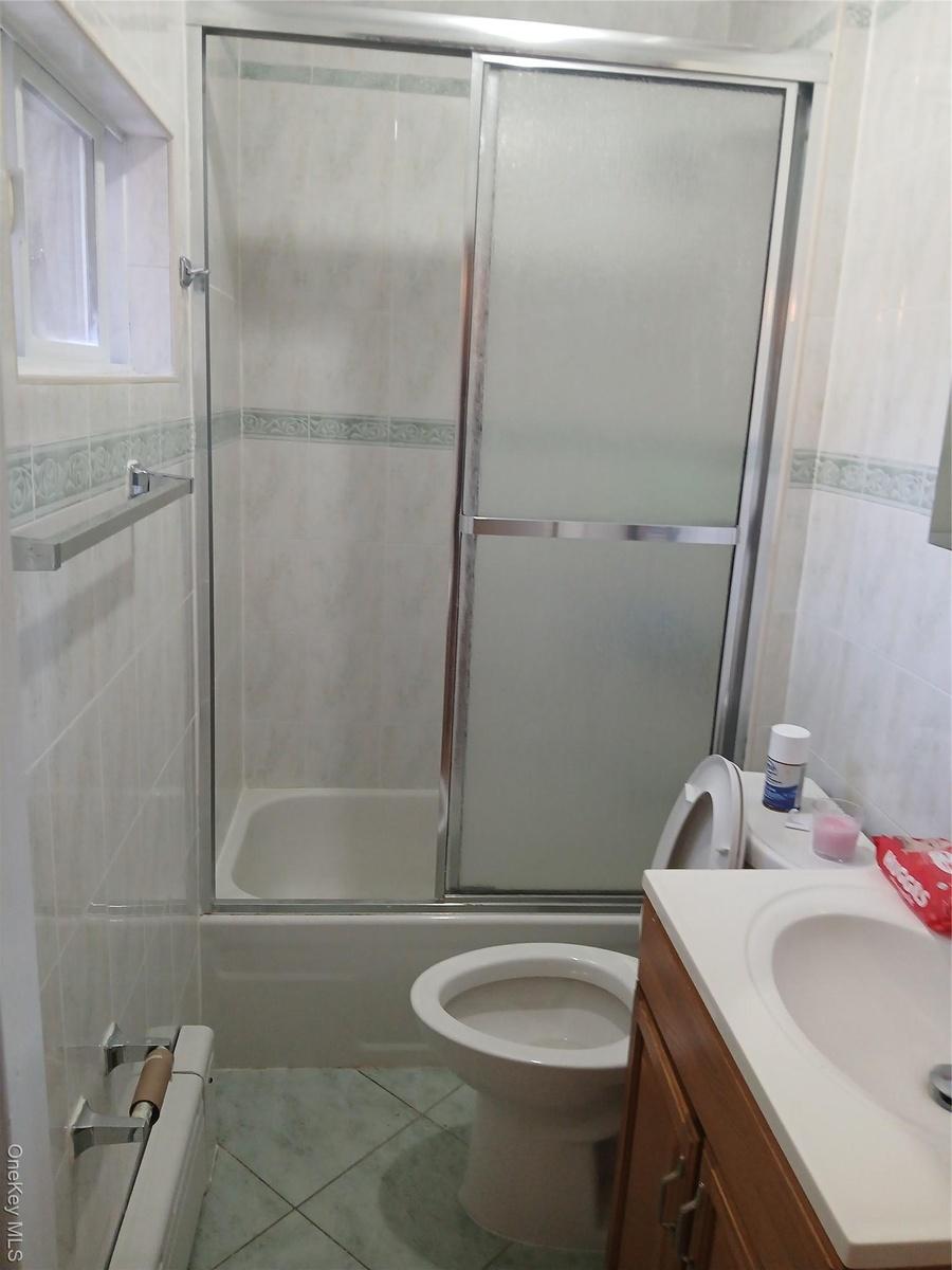 Bathroom featuring tile walls, vanity, light tile patterned floors, bath / shower combo with glass door, and a baseboard radiator