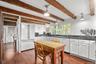 Kitchen featuring dark countertops, high end white refrigerator, beam ceiling, white cabinetry, and hanging light fixtures