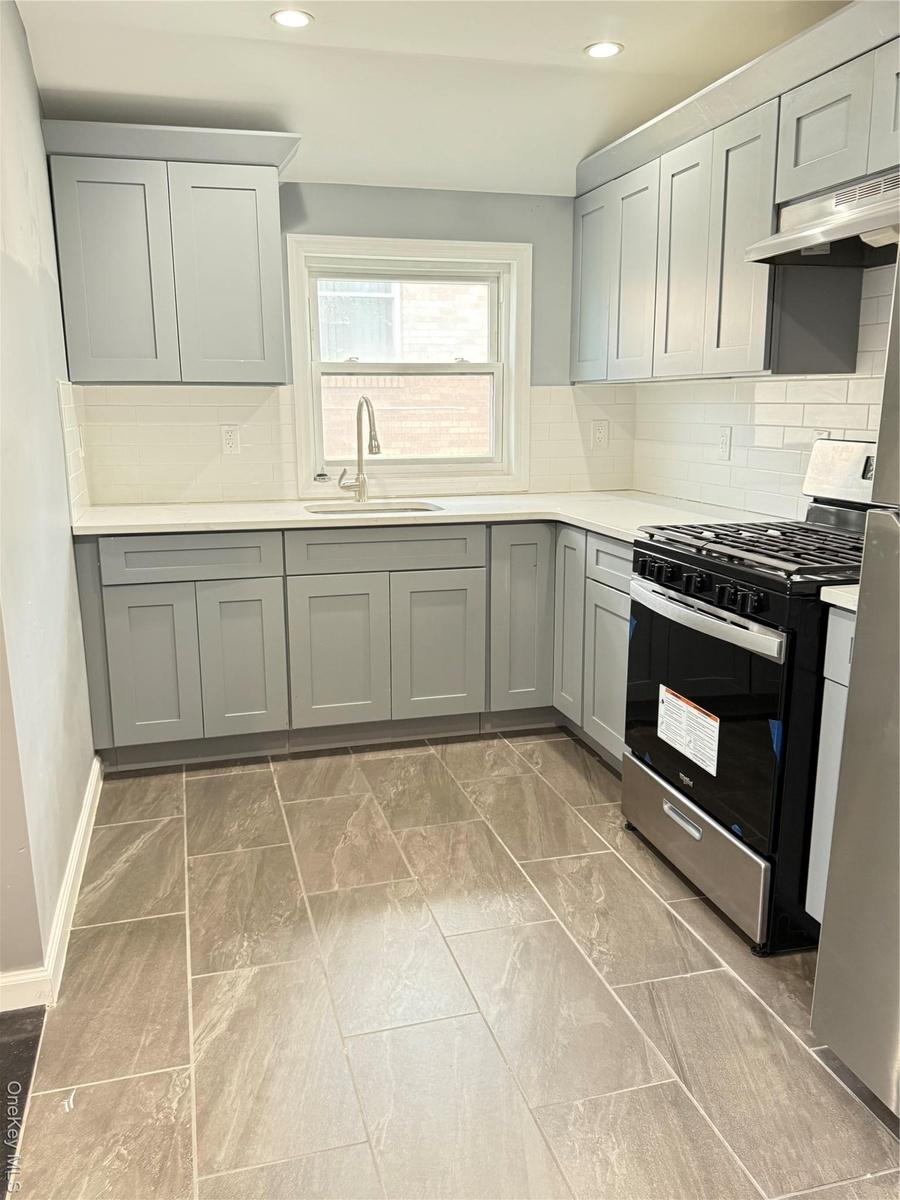 Kitchen with tasteful backsplash, gray cabinetry, stove, extractor fan, and recessed lighting