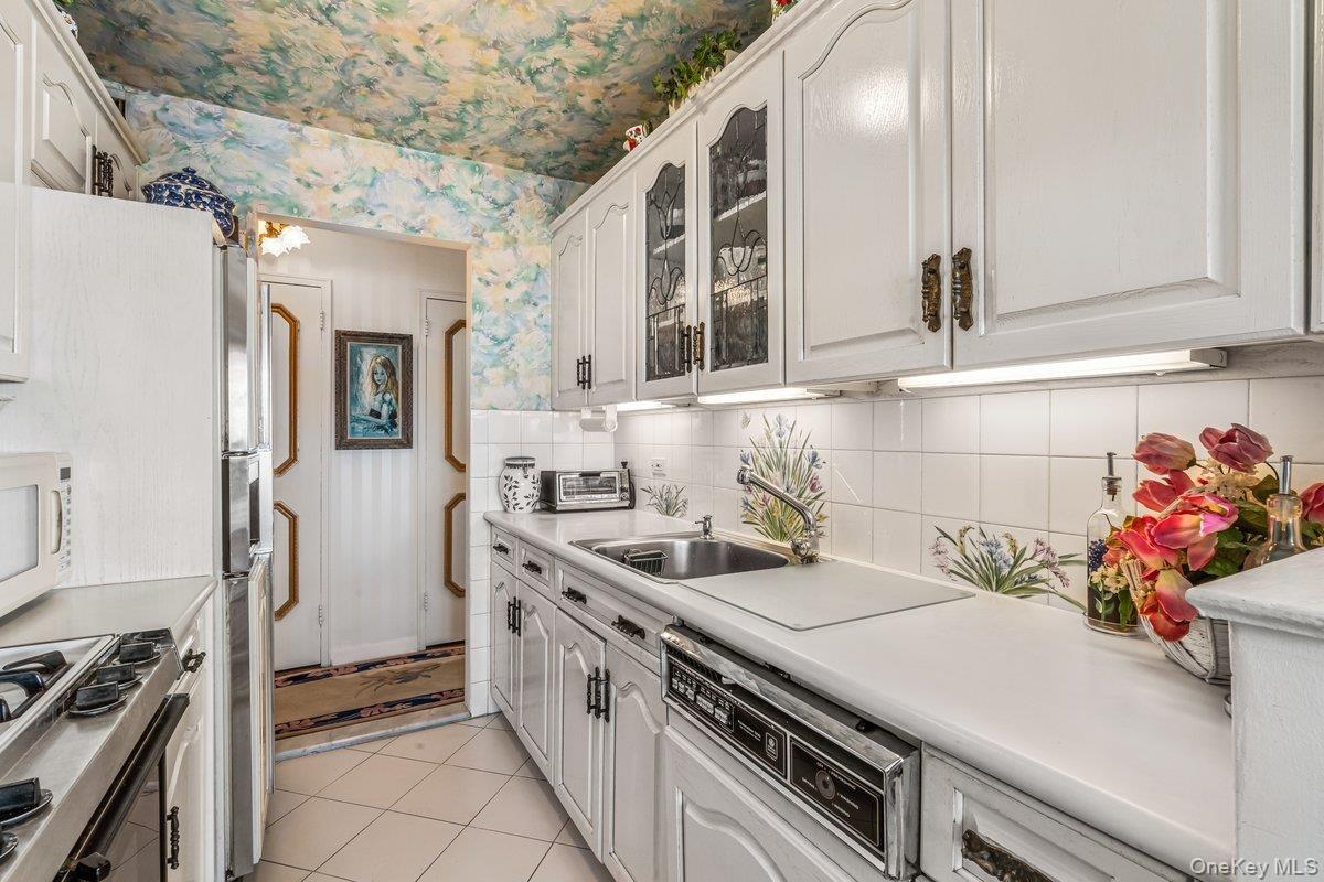 Kitchen with appliances with stainless steel finishes, light countertops, wallpapered walls, light tile patterned floors, and backsplash