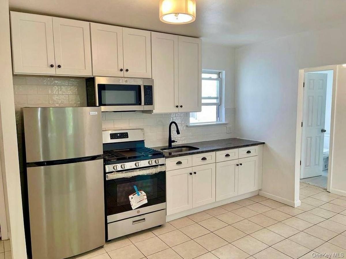Kitchen featuring appliances with stainless steel finishes, decorative backsplash, white cabinetry, light tile patterned floors, and dark stone counte