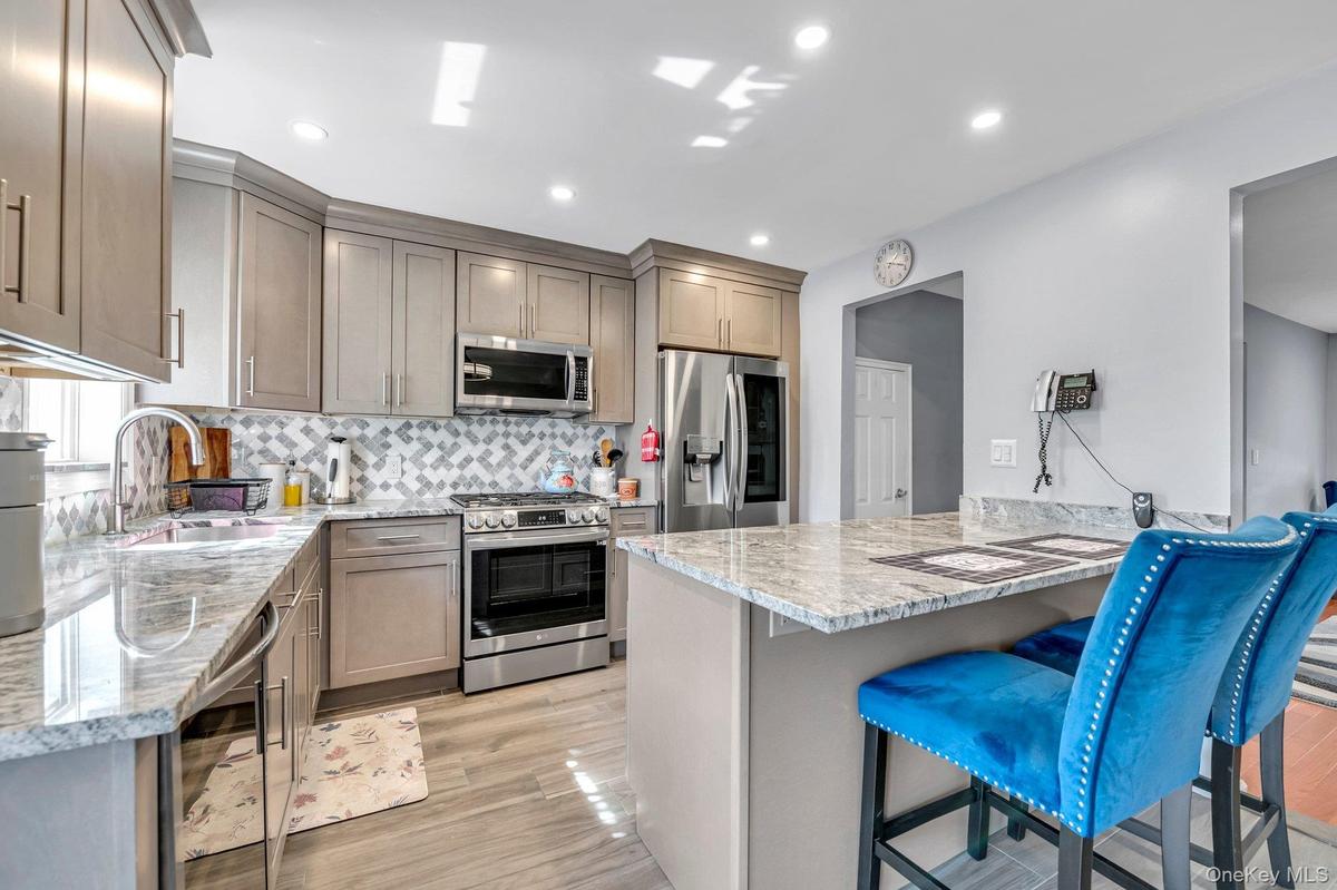 Kitchen with light stone counters, a breakfast bar, appliances with stainless steel finishes, decorative backsplash, and wine cooler