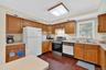 Kitchen with white appliances, light countertops, dark wood-style floors, under cabinet range hood, and brown cabinets
