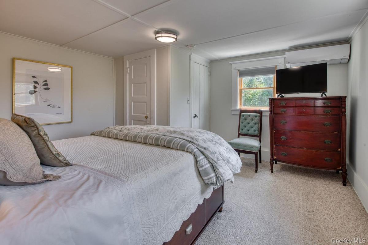 Bedroom with light colored carpet and an AC wall unit