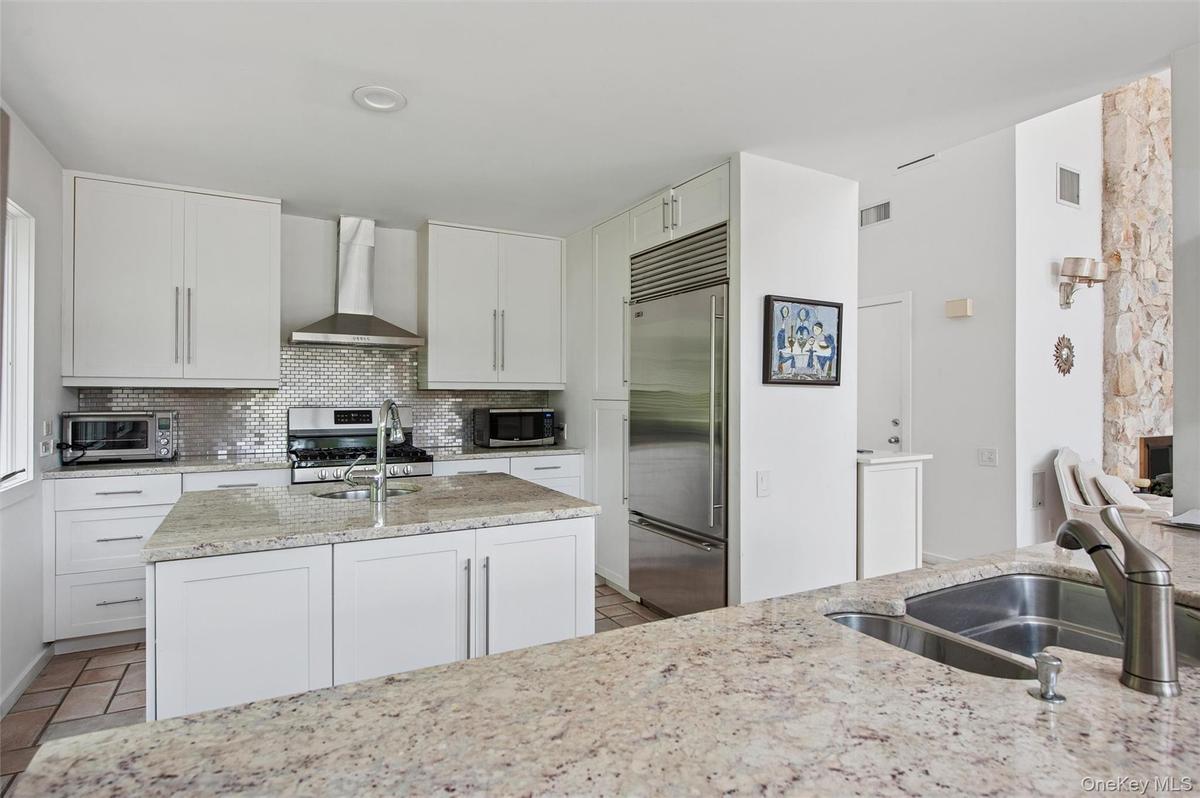 Kitchen with wall chimney exhaust hood, stainless steel appliances, light stone counters, and a sink