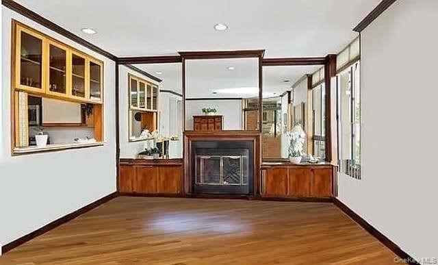 Unfurnished living room featuring a glass covered fireplace, wood finished floors, crown molding, and recessed lighting