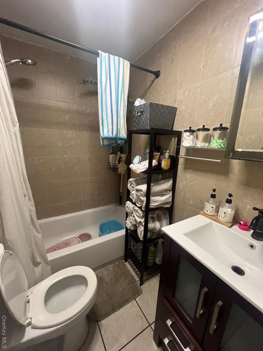 Bathroom with tile walls, shower / bath combo with shower curtain, vanity, and light tile patterned flooring