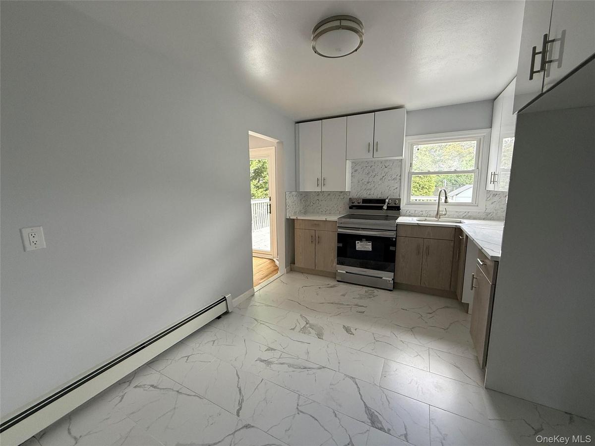 Kitchen featuring a baseboard heating unit, stainless steel electric stove, light marble finish flooring, decorative backsplash, and white cabinets