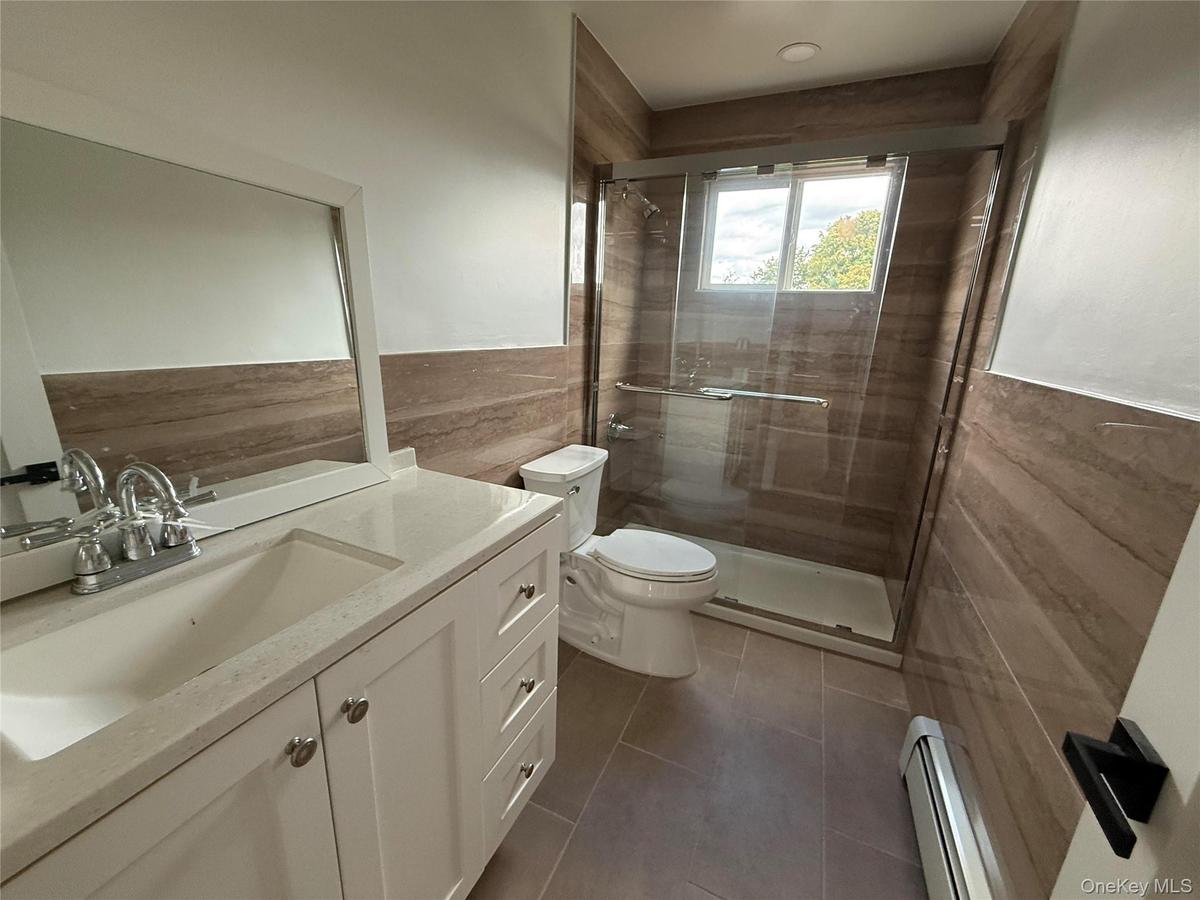 Full bathroom featuring tile walls, vanity, a baseboard heating unit, a shower stall, and dark tile patterned floors