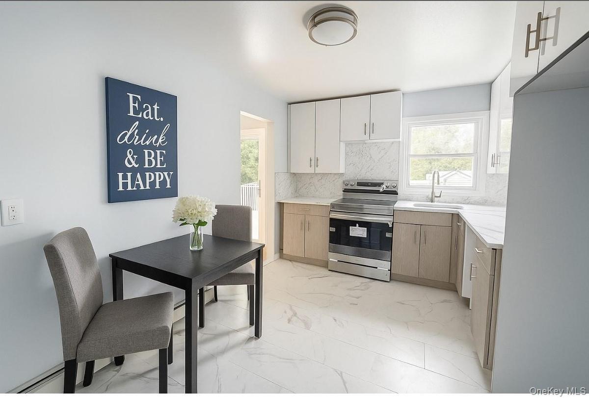 Kitchen featuring light marble finish flooring, electric stove, backsplash, a baseboard radiator, and white cabinetry