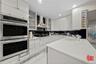 Kitchen with double oven, light countertops, white cabinets, wall chimney exhaust hood, and light marble finish flooring