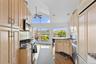Kitchen featuring appliances with stainless steel finishes, light brown cabinetry, lofted ceiling, light wood-style floors, and a peninsula
