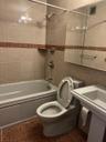 Bathroom featuring tiled shower / bath combo, toilet, and tile walls