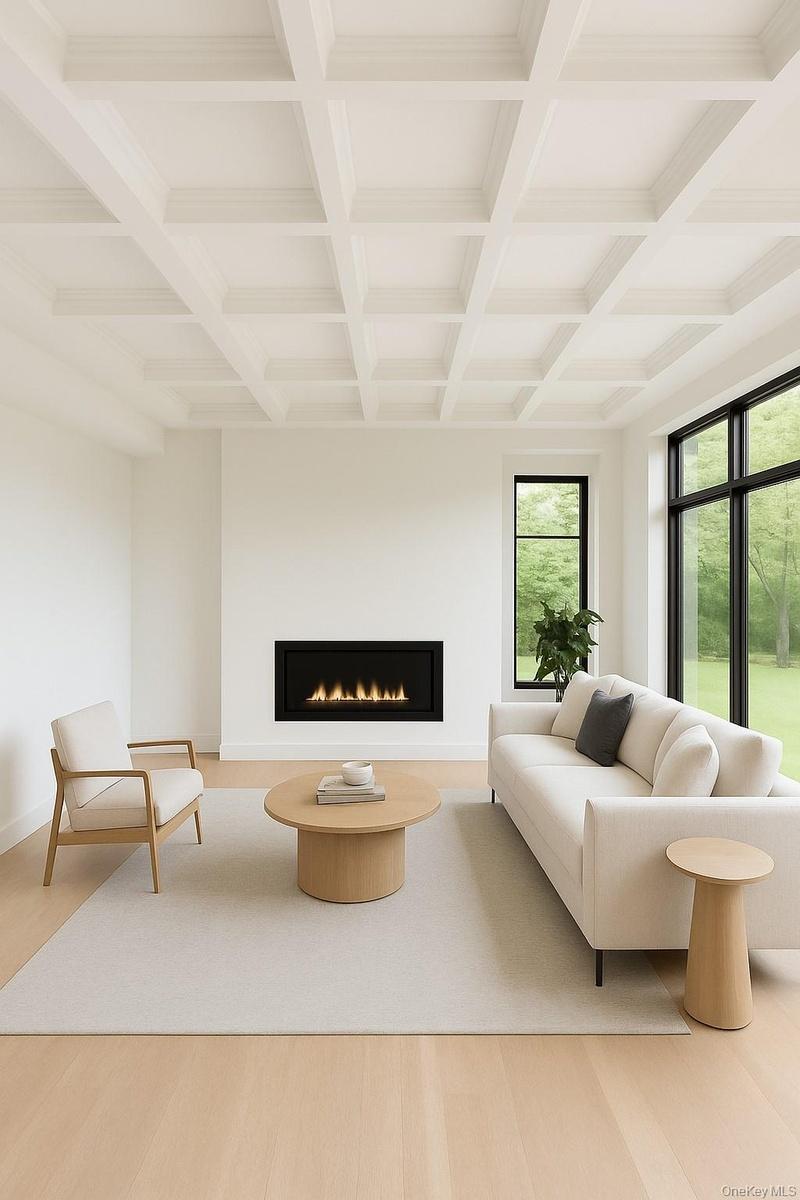 Living area featuring a warm lit fireplace, beamed ceiling, light wood-style floors, and coffered ceiling