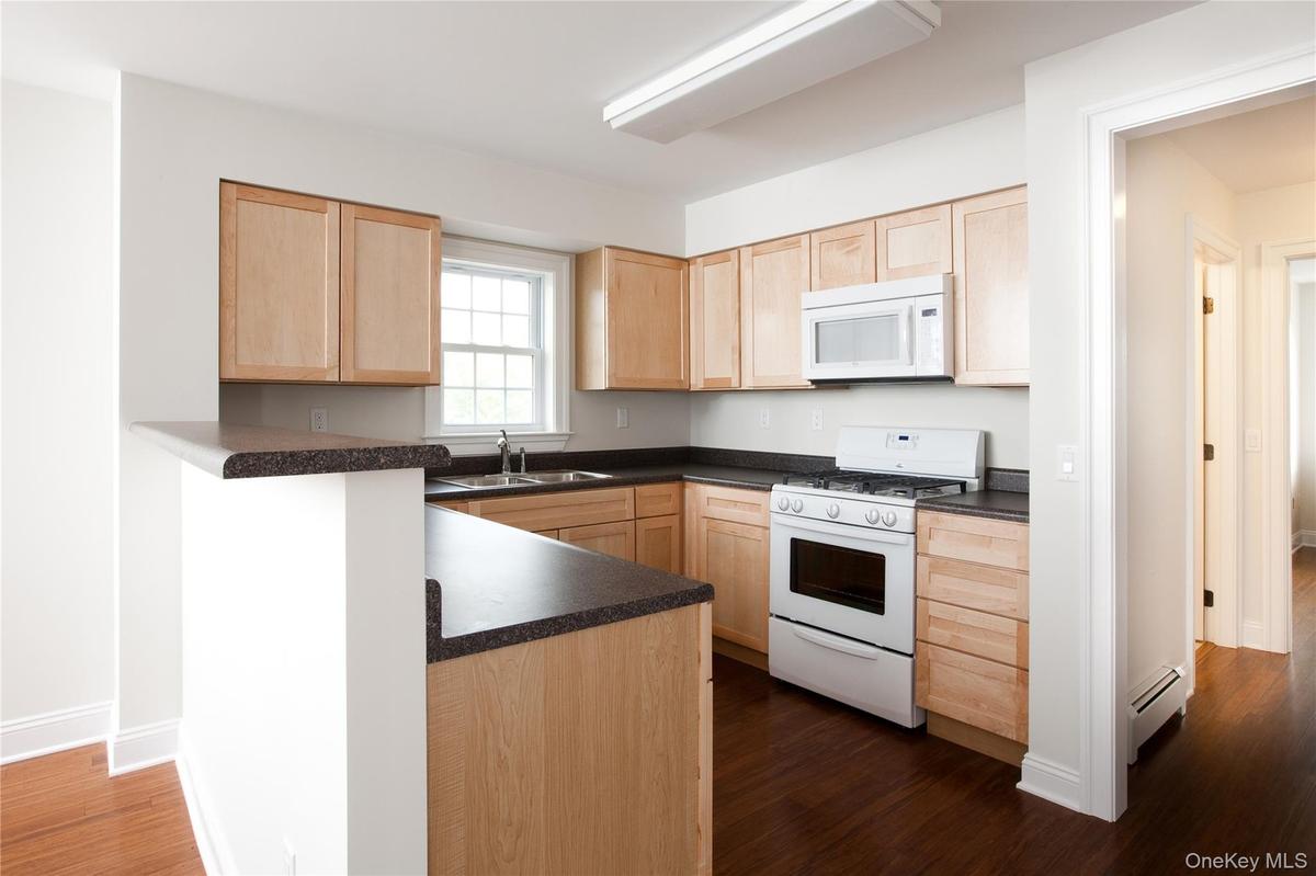 Kitchen with light brown cabinets, white appliances, dark countertops, and  wood-style flooring