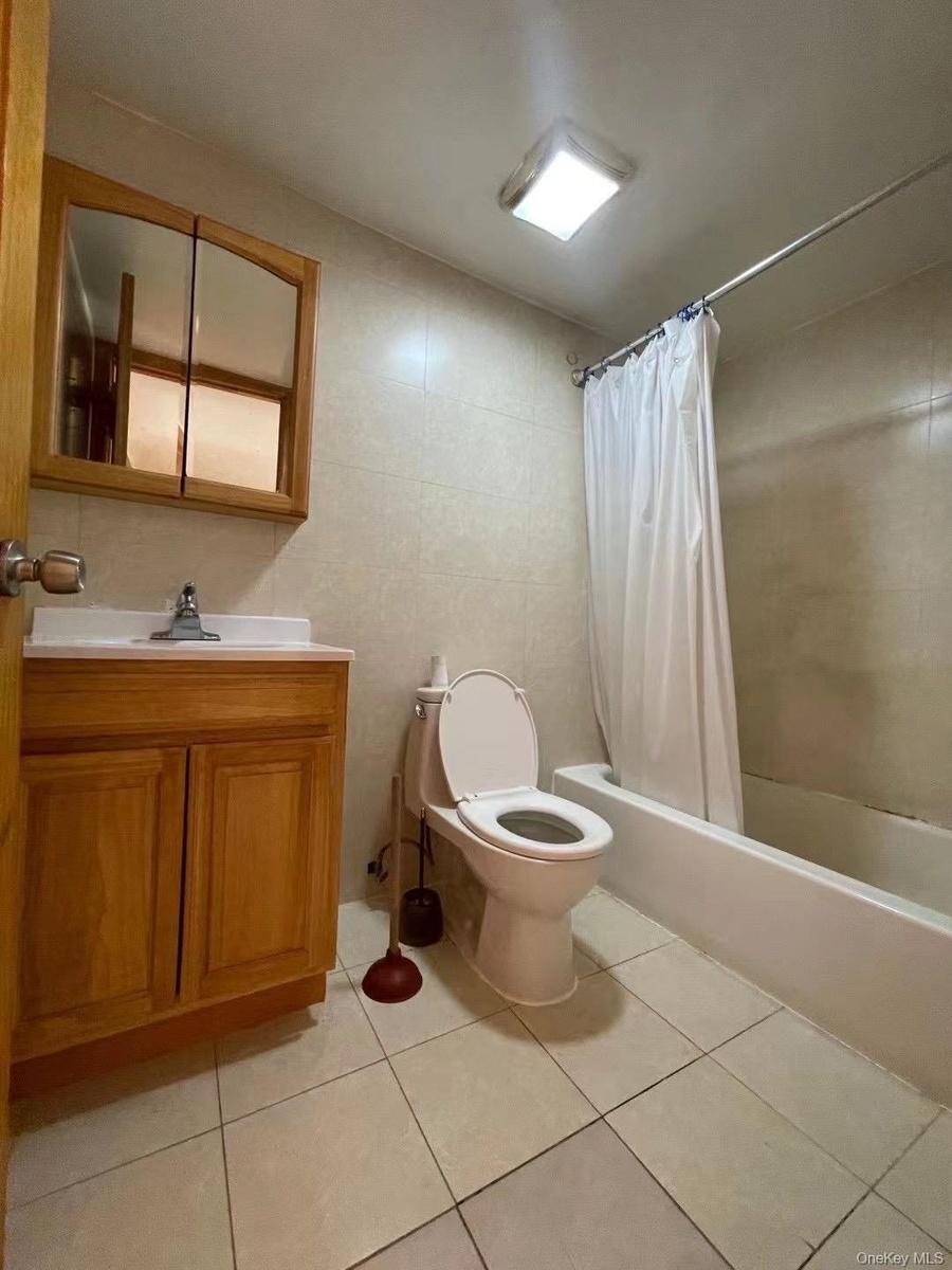 Bathroom with tile walls, shower / bath combo with shower curtain, vanity, and light tile patterned flooring