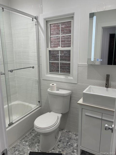 Bathroom with vanity, shower / bath combination with glass door, and tile walls
