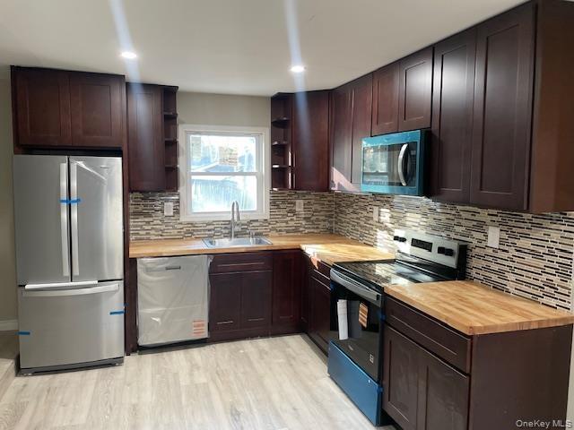 Kitchen with appliances with stainless steel finishes, dark brown cabinets, wooden counters, and recessed lighting