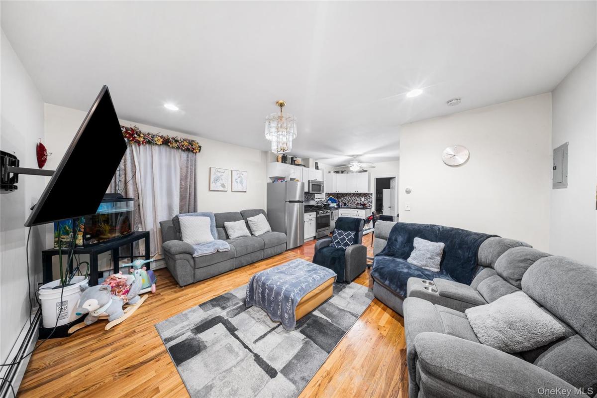 Living room featuring a chandelier, baseboard heating, light wood-style floors, a ceiling fan, and electric panel