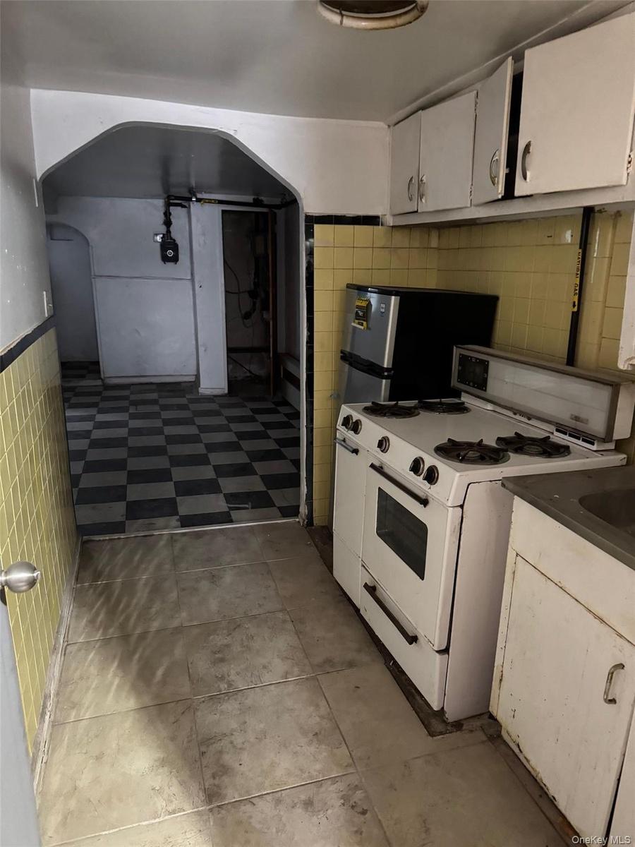 Kitchen with white range with gas cooktop, tile walls, white cabinetry, a wainscoted wall, and freestanding refrigerator