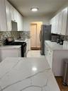 Kitchen with light stone counters, decorative backsplash, stainless steel appliances, white cabinetry, and light wood finished floors
