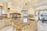 Kitchen with cream cabinetry, a chandelier, ornamental molding, light stone counters, and backsplash