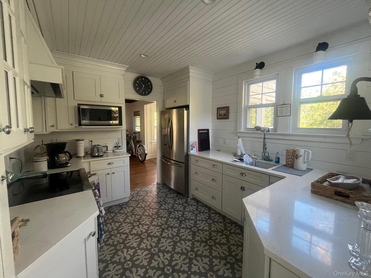 Kitchen with white cabinetry, appliances with stainless steel finishes, premium range hood, light stone counters, and wood ceiling