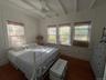 Bedroom with beam ceiling, multiple windows, dark wood-style flooring, ceiling fan, and a decorative wall