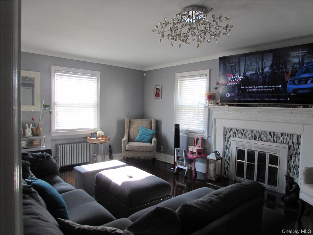 Living room featuring radiator, plenty of natural light, wood finished floors, a tiled fireplace, and crown molding