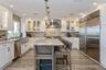 Kitchen featuring wall chimney exhaust hood, light stone counters, a kitchen island, and appliances with stainless steel finishes