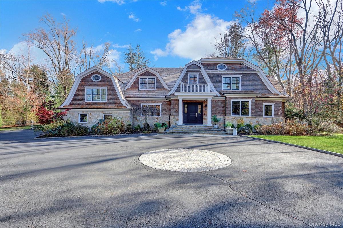 Shingle-style home featuring a gambrel roof, stone siding, and curved driveway