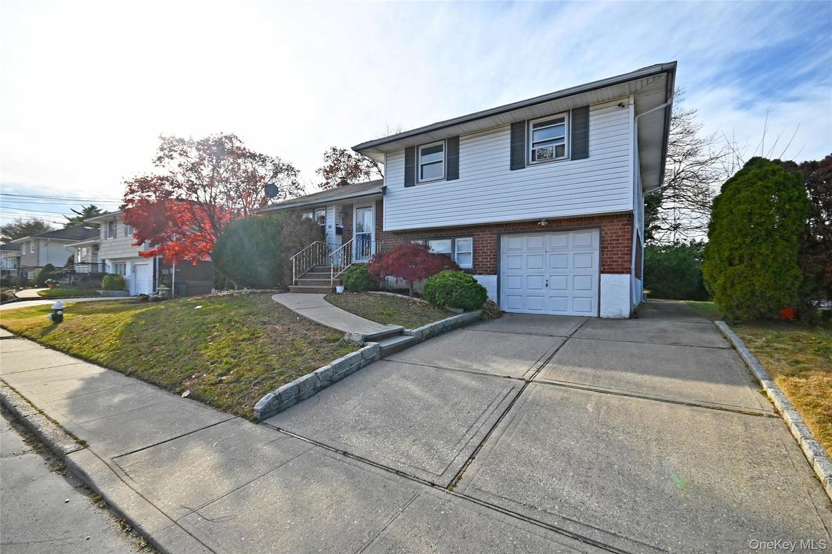 Split level home featuring brick siding, driveway, an attached garage, and a front lawn