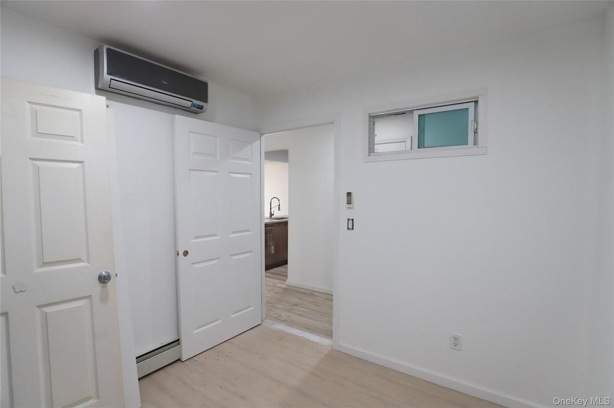 Interior room featuring wood-finish flooring, a wall-mounted ductless climate control unit, a sliding-door closet, and a horizontal transom window